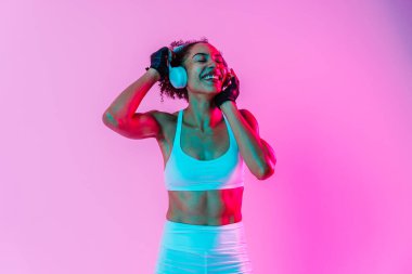 Sportif siyahi kadın spor kıyafetleri giyiyor spor salonunda, renkli dramatik ışıklandırma - spor yapan Afro-Amerikan bayan sporcu