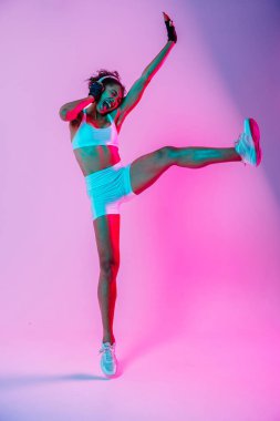 Sportif siyahi kadın spor kıyafetleri giyiyor spor salonunda, renkli dramatik ışıklandırma - spor yapan Afro-Amerikan bayan sporcu