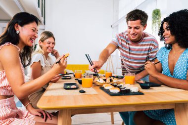 Çok ırklı bir grup genç arkadaş evde buluşup suşi yiyorlar. Çok ırklı mutlu insanlar öğle yemeği yerken kaynaşıyorlar.