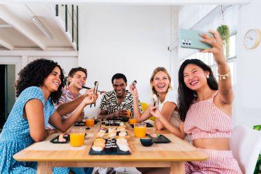 Çok ırklı bir grup genç arkadaş evde buluşup suşi yiyorlar. Çok ırklı mutlu insanlar öğle yemeği yerken kaynaşıyorlar.