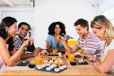 Çok ırklı bir grup genç arkadaş evde buluşup suşi yiyorlar. Çok ırklı mutlu insanlar öğle yemeği yerken kaynaşıyorlar.