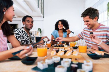 Çok ırklı bir grup genç arkadaş evde buluşup suşi yiyorlar. Çok ırklı mutlu insanlar öğle yemeği yerken kaynaşıyorlar.