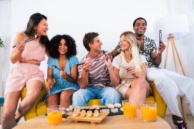 Çok ırklı bir grup genç arkadaş evde buluşup suşi yiyorlar. Çok ırklı mutlu insanlar öğle yemeği yerken kaynaşıyorlar.