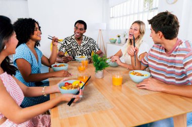Çok ırklı bir grup genç arkadaş evde buluşuyor ve yemek yerken çok ırklı ve mutlu insanlar yemek yiyor.