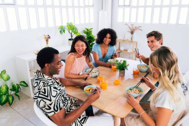 Çok ırklı bir grup genç arkadaş evde buluşuyor ve yemek yerken çok ırklı ve mutlu insanlar yemek yiyor.