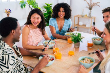 Çok ırklı bir grup genç arkadaş evde buluşuyor ve yemek yerken çok ırklı ve mutlu insanlar yemek yiyor.