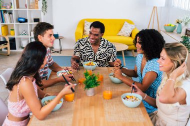 Çok ırklı bir grup genç arkadaş evde buluşuyor ve yemek yerken çok ırklı ve mutlu insanlar yemek yiyor.