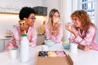 Evde pijama partisi sırasında kahvaltı eden çok ırklı bir grup genç kız arkadaş mutlu mutlu en iyi arkadaşlar kaynaşıyor ve evde eğleniyorlar.