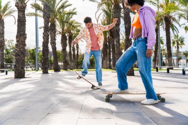 Açık havada kaykay yapan çok ırklı genç bir çift - iki arkadaş şehir bölgelerinde kayak yaparken eğleniyor, gençlik, çeşitlilik, yeşil traksiyonlar ve hareketlilik kavramları