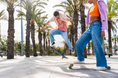 Açık havada kaykay yapan çok ırklı genç bir çift - iki arkadaş şehir bölgelerinde kayak yaparken eğleniyor, gençlik, çeşitlilik, yeşil traksiyonlar ve hareketlilik kavramları