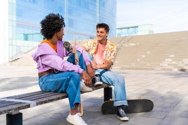 Açık havada kaykay yapan çok ırklı genç bir çift - iki arkadaş şehir bölgelerinde kayak yaparken eğleniyor, gençlik, çeşitlilik, yeşil traksiyonlar ve hareketlilik kavramları