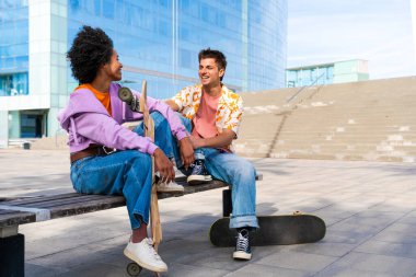 Açık havada kaykay yapan çok ırklı genç bir çift - iki arkadaş şehir bölgelerinde kayak yaparken eğleniyor, gençlik, çeşitlilik, yeşil traksiyonlar ve hareketlilik kavramları