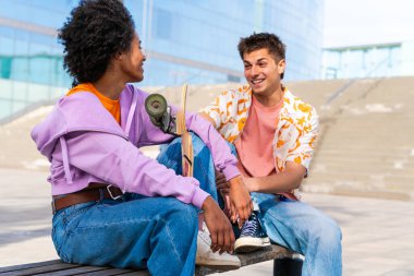 Açık havada kaykay yapan çok ırklı genç bir çift - iki arkadaş şehir bölgelerinde kayak yaparken eğleniyor, gençlik, çeşitlilik, yeşil traksiyonlar ve hareketlilik kavramları