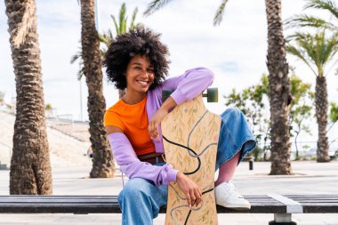 Açık havada kıvırcık saçlı güzel siyahi bir kadın modern havalı kadın şık şehir kıyafetleri içinde şehirde geziyor.