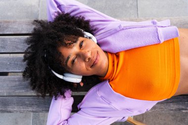 Açık havada kıvırcık saçlı güzel siyahi bir kadın modern havalı kadın şık şehir kıyafetleri giyiyor şehirde kaykayla geziyor.