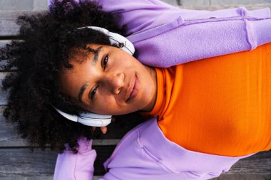 Açık havada kıvırcık saçlı güzel siyahi bir kadın modern havalı kadın şık şehir kıyafetleri giyiyor şehirde kaykayla geziyor.