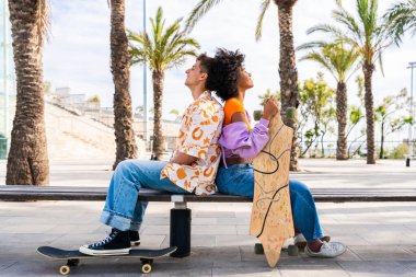 Açık havada kaykay yapan çok ırklı genç bir çift - iki arkadaş şehir bölgelerinde kayak yaparken eğleniyor, gençlik, çeşitlilik, yeşil traksiyonlar ve hareketlilik kavramları