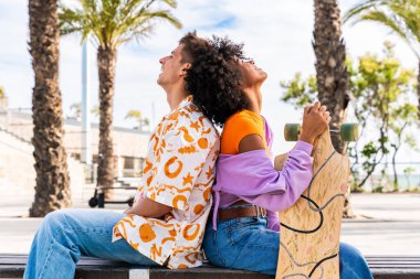 Açık havada kaykay yapan çok ırklı genç bir çift - iki arkadaş şehir bölgelerinde kayak yaparken eğleniyor, gençlik, çeşitlilik, yeşil traksiyonlar ve hareketlilik kavramları