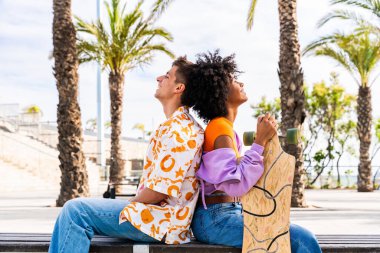 Açık havada kaykay yapan çok ırklı genç bir çift - iki arkadaş şehir bölgelerinde kayak yaparken eğleniyor, gençlik, çeşitlilik, yeşil traksiyonlar ve hareketlilik kavramları