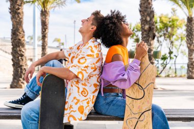 Açık havada kaykay yapan çok ırklı genç bir çift - iki arkadaş şehir bölgelerinde kayak yaparken eğleniyor, gençlik, çeşitlilik, yeşil traksiyonlar ve hareketlilik kavramları