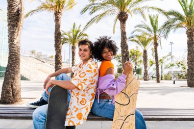 Açık havada kaykay yapan çok ırklı genç bir çift - iki arkadaş şehir bölgelerinde kayak yaparken eğleniyor, gençlik, çeşitlilik, yeşil traksiyonlar ve hareketlilik kavramları