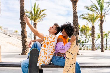 Açık havada kaykay yapan çok ırklı genç bir çift - iki arkadaş şehir bölgelerinde kayak yaparken eğleniyor, gençlik, çeşitlilik, yeşil traksiyonlar ve hareketlilik kavramları