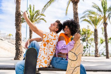 Açık havada kaykay yapan çok ırklı genç bir çift - iki arkadaş şehir bölgelerinde kayak yaparken eğleniyor, gençlik, çeşitlilik, yeşil traksiyonlar ve hareketlilik kavramları