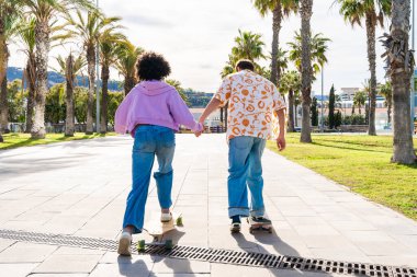 Açık havada kaykay yapan çok ırklı genç bir çift - iki arkadaş şehir bölgelerinde kayak yaparken eğleniyor, gençlik, çeşitlilik, yeşil traksiyonlar ve hareketlilik kavramları