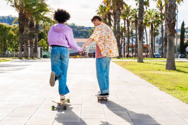 Açık havada kaykay yapan çok ırklı genç bir çift - iki arkadaş şehir bölgelerinde kayak yaparken eğleniyor, gençlik, çeşitlilik, yeşil traksiyonlar ve hareketlilik kavramları