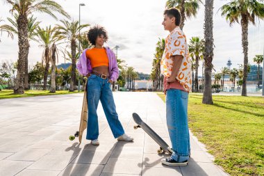 Açık havada kaykay yapan çok ırklı genç bir çift - iki arkadaş şehir bölgelerinde kayak yaparken eğleniyor, gençlik, çeşitlilik, yeşil traksiyonlar ve hareketlilik kavramları