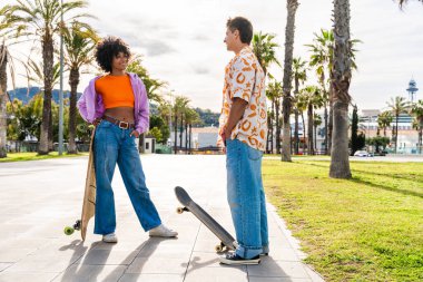 Açık havada kaykay yapan çok ırklı genç bir çift - iki arkadaş şehir bölgelerinde kayak yaparken eğleniyor, gençlik, çeşitlilik, yeşil traksiyonlar ve hareketlilik kavramları