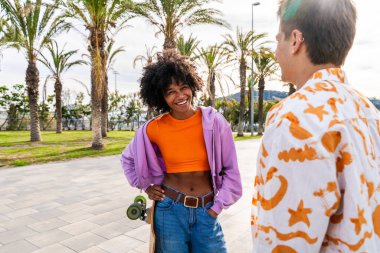 Açık havada kaykay yapan çok ırklı genç bir çift - iki arkadaş şehir bölgelerinde kayak yaparken eğleniyor, gençlik, çeşitlilik, yeşil traksiyonlar ve hareketlilik kavramları