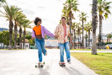 Açık havada kaykay yapan çok ırklı genç bir çift - iki arkadaş şehir bölgelerinde kayak yaparken eğleniyor, gençlik, çeşitlilik, yeşil traksiyonlar ve hareketlilik kavramları