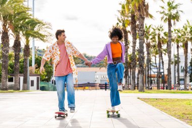 Açık havada kaykay yapan çok ırklı genç bir çift - iki arkadaş şehir bölgelerinde kayak yaparken eğleniyor, gençlik, çeşitlilik, yeşil traksiyonlar ve hareketlilik kavramları