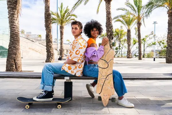 Açık havada kaykay yapan çok ırklı genç bir çift - iki arkadaş şehir bölgelerinde kayak yaparken eğleniyor, gençlik, çeşitlilik, yeşil traksiyonlar ve hareketlilik kavramları