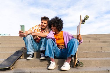 Açık havada kaykay yapan çok ırklı genç bir çift - iki arkadaş şehir bölgelerinde kayak yaparken eğleniyor, gençlik, çeşitlilik, yeşil traksiyonlar ve hareketlilik kavramları