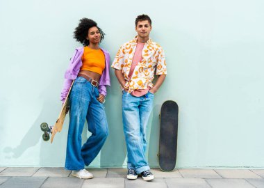 Açık havada kaykay yapan çok ırklı genç bir çift - iki arkadaş şehir bölgelerinde kayak yaparken eğleniyor, gençlik, çeşitlilik, yeşil traksiyonlar ve hareketlilik kavramları