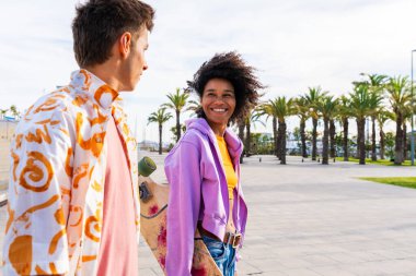 Açık havada kaykay yapan çok ırklı genç bir çift - iki arkadaş şehir bölgelerinde kayak yaparken eğleniyor, gençlik, çeşitlilik, yeşil traksiyonlar ve hareketlilik kavramları