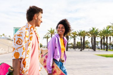 Açık havada kaykay yapan çok ırklı genç bir çift - iki arkadaş şehir bölgelerinde kayak yaparken eğleniyor, gençlik, çeşitlilik, yeşil traksiyonlar ve hareketlilik kavramları