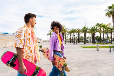 Açık havada kaykay yapan çok ırklı genç bir çift - iki arkadaş şehir bölgelerinde kayak yaparken eğleniyor, gençlik, çeşitlilik, yeşil traksiyonlar ve hareketlilik kavramları