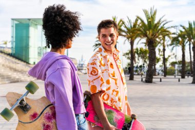 Açık havada kaykay yapan çok ırklı genç bir çift - iki arkadaş şehir bölgelerinde kayak yaparken eğleniyor, gençlik, çeşitlilik, yeşil traksiyonlar ve hareketlilik kavramları