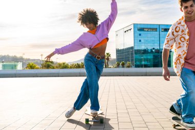 Açık havada kaykay yapan çok ırklı genç bir çift - iki arkadaş şehir bölgelerinde kayak yaparken eğleniyor, gençlik, çeşitlilik, yeşil traksiyonlar ve hareketlilik kavramları