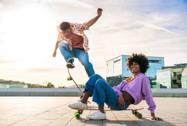 Açık havada kaykay yapan çok ırklı genç bir çift - iki arkadaş şehir bölgelerinde kayak yaparken eğleniyor, gençlik, çeşitlilik, yeşil traksiyonlar ve hareketlilik kavramları