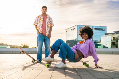 Açık havada kaykay yapan çok ırklı genç bir çift - iki arkadaş şehir bölgelerinde kayak yaparken eğleniyor, gençlik, çeşitlilik, yeşil traksiyonlar ve hareketlilik kavramları