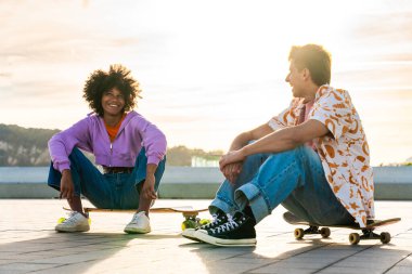 Açık havada kaykay yapan çok ırklı genç bir çift - iki arkadaş şehir bölgelerinde kayak yaparken eğleniyor, gençlik, çeşitlilik, yeşil traksiyonlar ve hareketlilik kavramları