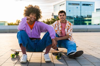 Açık havada kaykay yapan çok ırklı genç bir çift - iki arkadaş şehir bölgelerinde kayak yaparken eğleniyor, gençlik, çeşitlilik, yeşil traksiyonlar ve hareketlilik kavramları