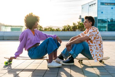 Açık havada kaykay yapan çok ırklı genç bir çift - iki arkadaş şehir bölgelerinde kayak yaparken eğleniyor, gençlik, çeşitlilik, yeşil traksiyonlar ve hareketlilik kavramları