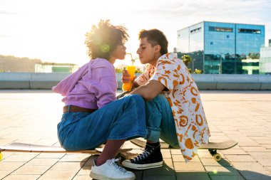 Açık havada kaykay yapan çok ırklı genç bir çift - iki arkadaş şehir bölgelerinde kayak yaparken eğleniyor, gençlik, çeşitlilik, yeşil traksiyonlar ve hareketlilik kavramları