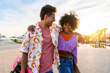 Açık havada kaykay yapan çok ırklı genç bir çift - iki arkadaş şehir bölgelerinde kayak yaparken eğleniyor, gençlik, çeşitlilik, yeşil traksiyonlar ve hareketlilik kavramları