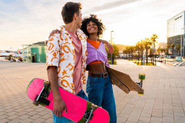 Açık havada kaykay yapan çok ırklı genç bir çift - iki arkadaş şehir bölgelerinde kayak yaparken eğleniyor, gençlik, çeşitlilik, yeşil traksiyonlar ve hareketlilik kavramları